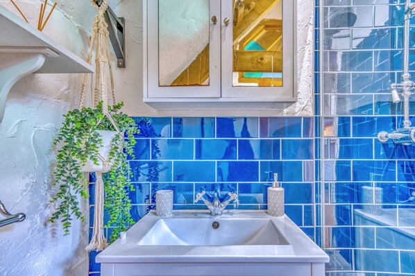 Ein Badezimmer mit einem weißen Waschbecken, blautonierten Fliesen, einem weißen Schrank und einer hängenden Pflanze.