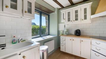 A kitchen with white cabinets, a window, a sink, and a coffee maker.