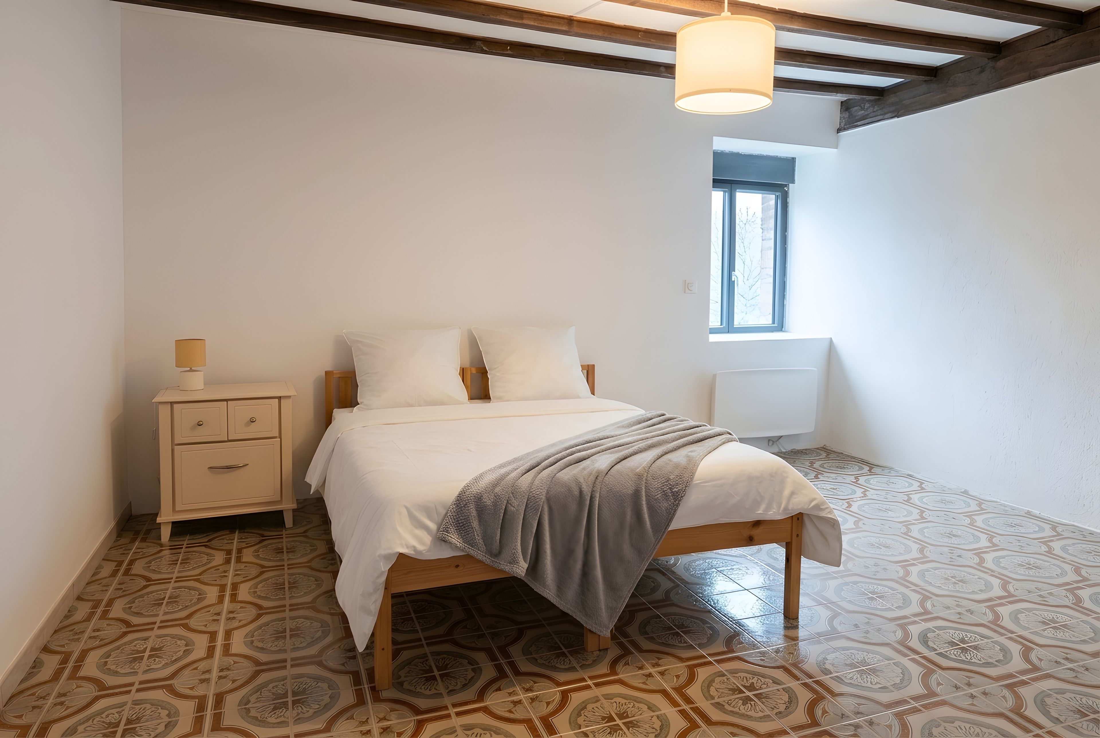 A bedroom with a bed, bedside table, lamp, and a window.
