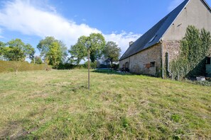 A stone building with a sloped roof, surrounded by a grassy field and trees.
