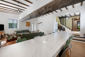 A spacious living area with a large white table, green sofas, and a wooden ceiling beam.