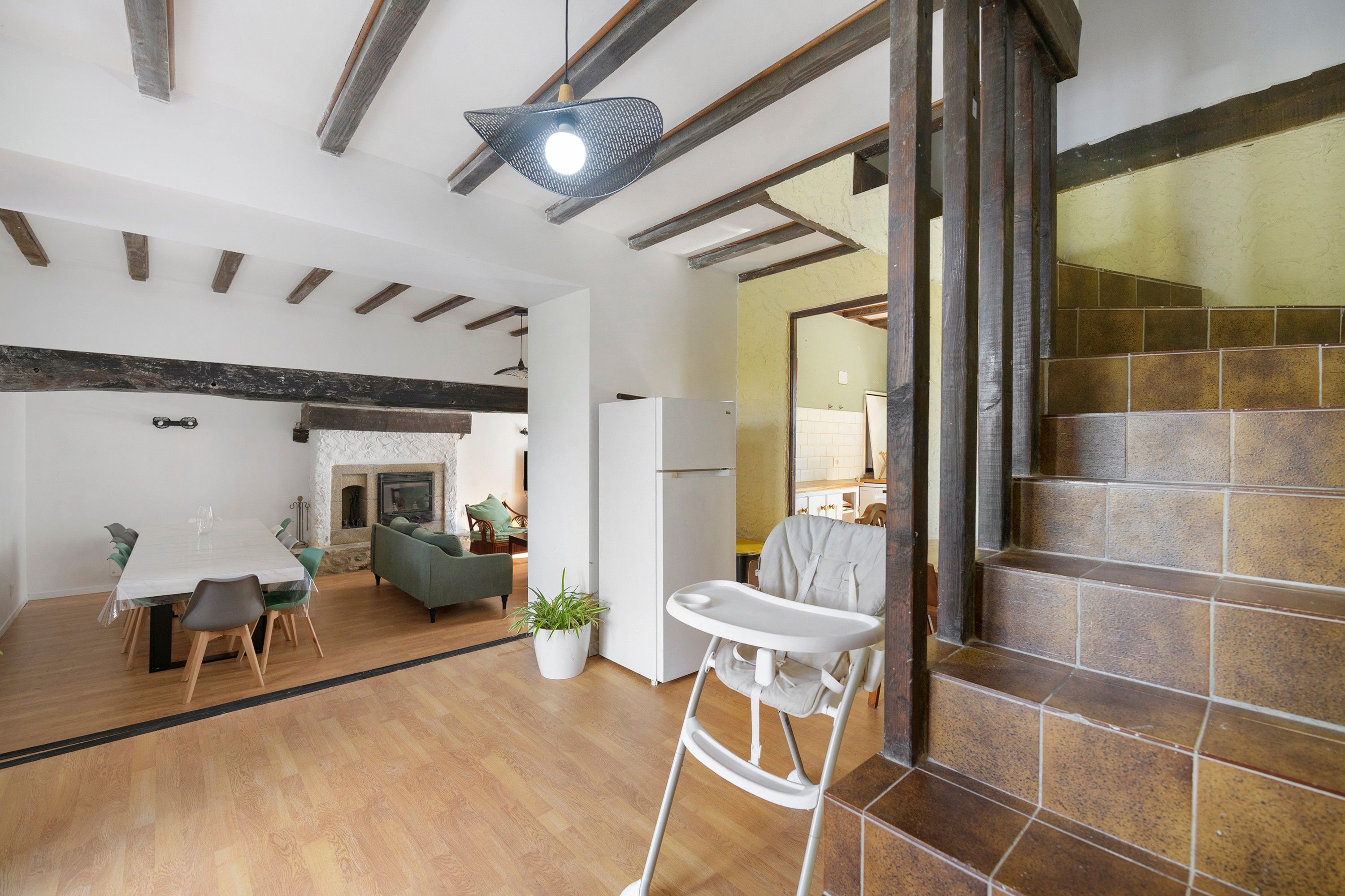 A spacious living area with a dining table, chairs, a sofa, a baby chair, and a fireplace.