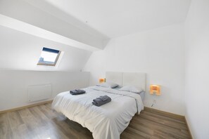 A bedroom with a sloped ceiling, a skylight, a bed with white bedding, two bedside lamps, and a radiator.
