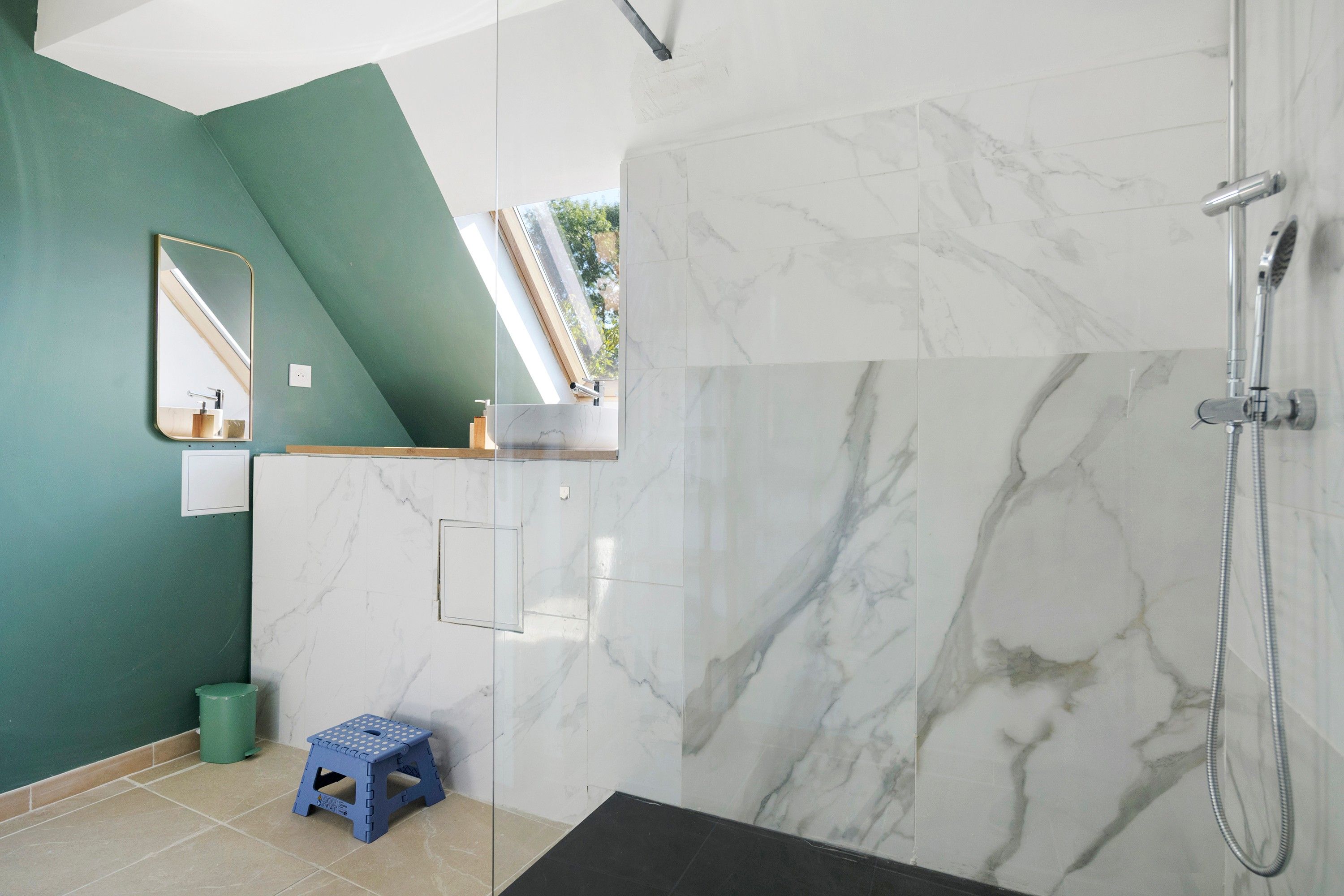 A bathroom with a shower, a mirror, and a green wall.