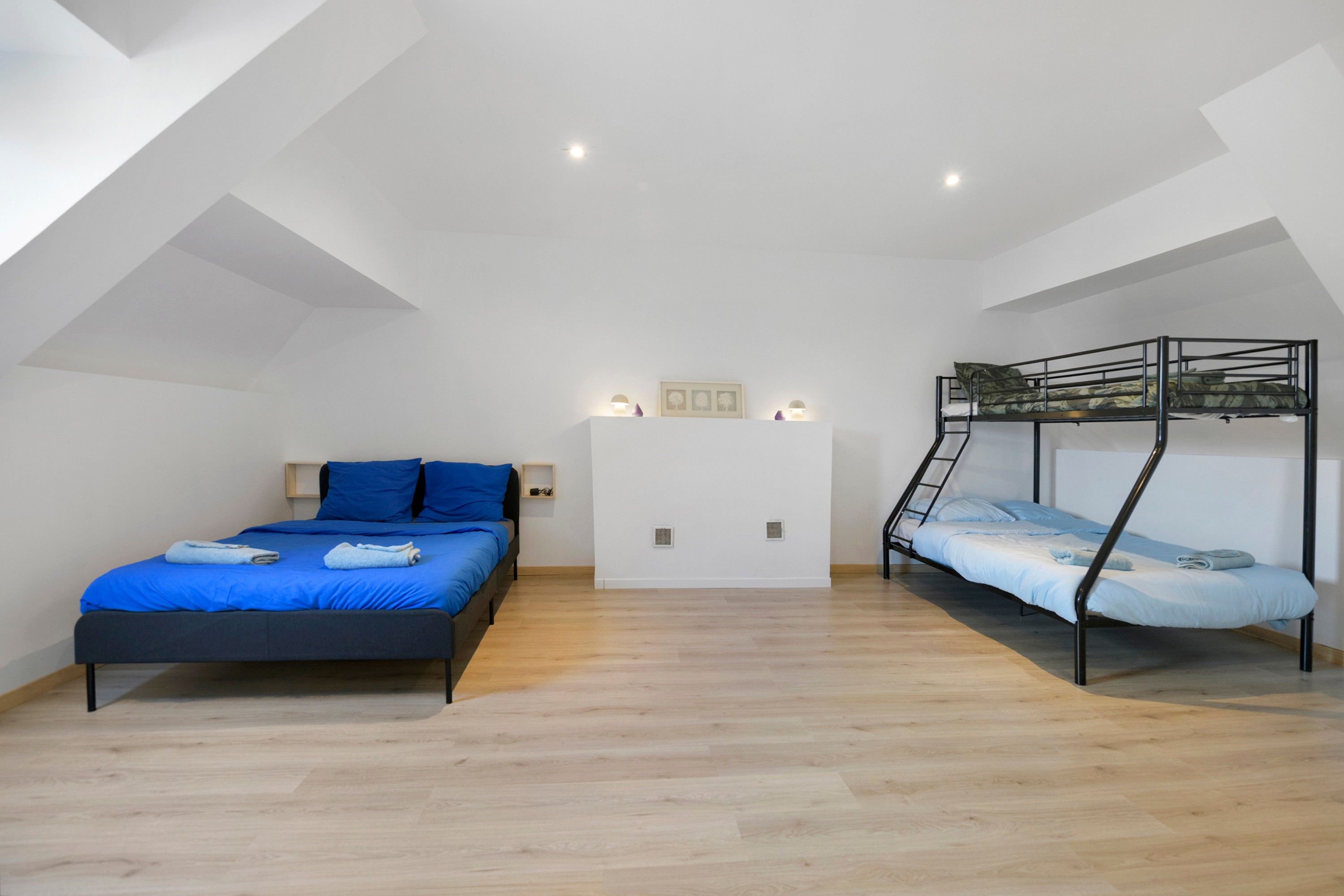 A room with a single bed, a bunk bed, wooden flooring, and a sloped ceiling.