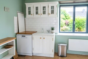 Une cuisine compacte avec des meubles blancs, un lave-vaisselle et une fenêtre donnant sur un espace verdoyant.
