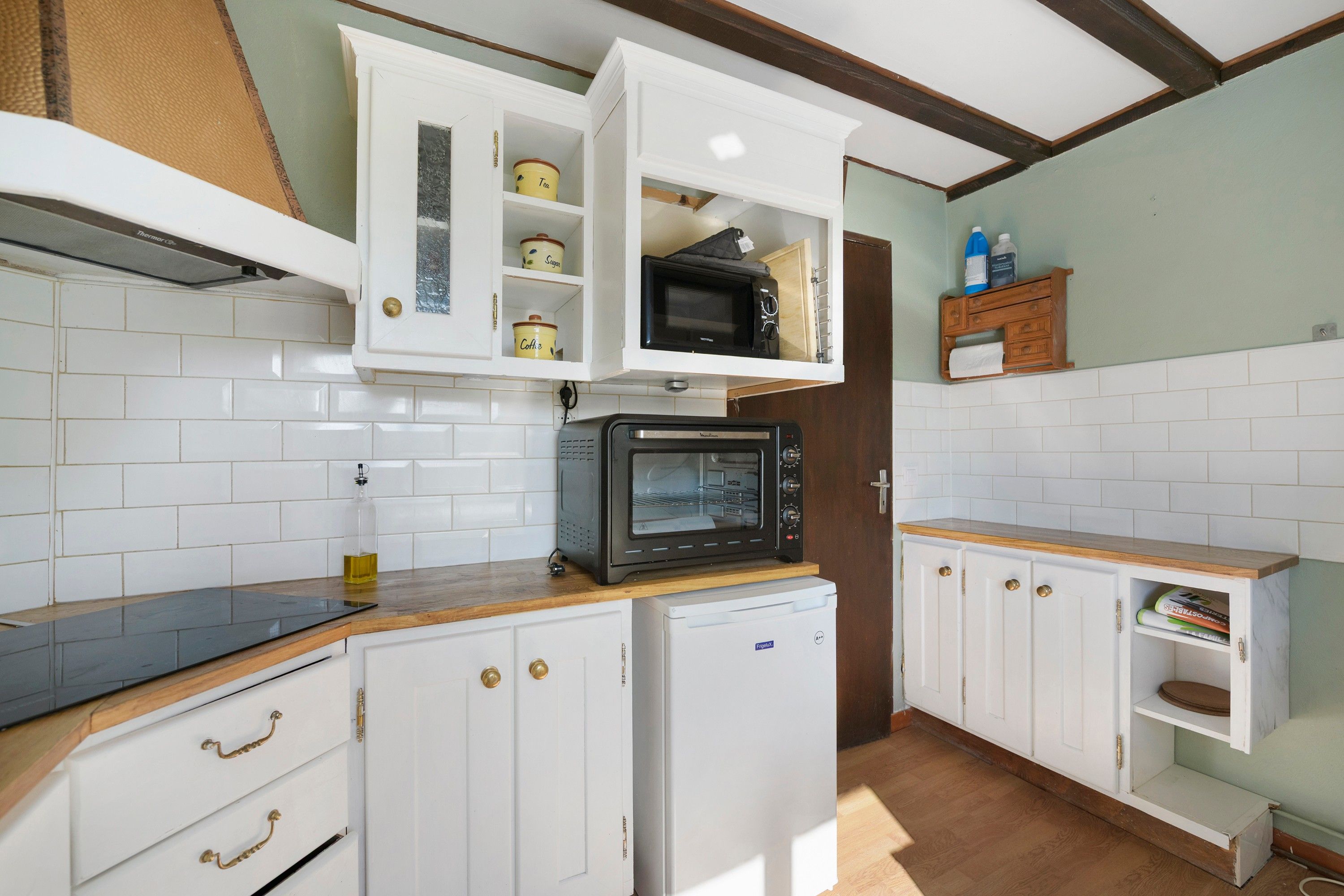A compact kitchen with white cabinets, a black microwave, and a small refrigerator.
