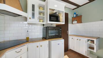 A compact kitchen with white cabinets, a black microwave, and a small refrigerator.