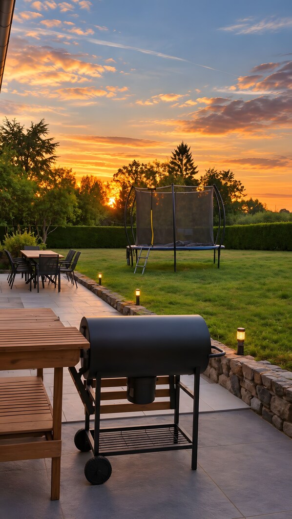 Un espace extérieur aménagé avec un barbecue, des sièges et un trampoline.