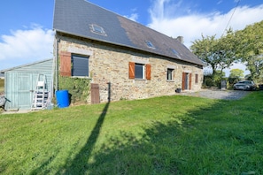 A stone house with a sloped roof, a small attached shed, and a car parked in the driveway.