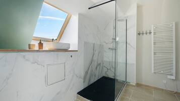A modern bathroom with a glass shower enclosure, a white sink, and a window providing natural light.