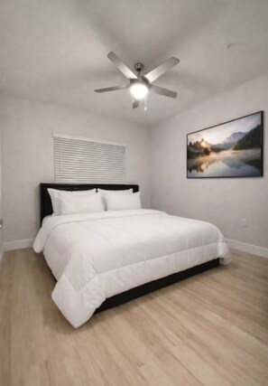 Une chambre à coucher avec un lit, un ventilateur de plafond, une fenêtre avec des stores et un tableau accroché au mur.