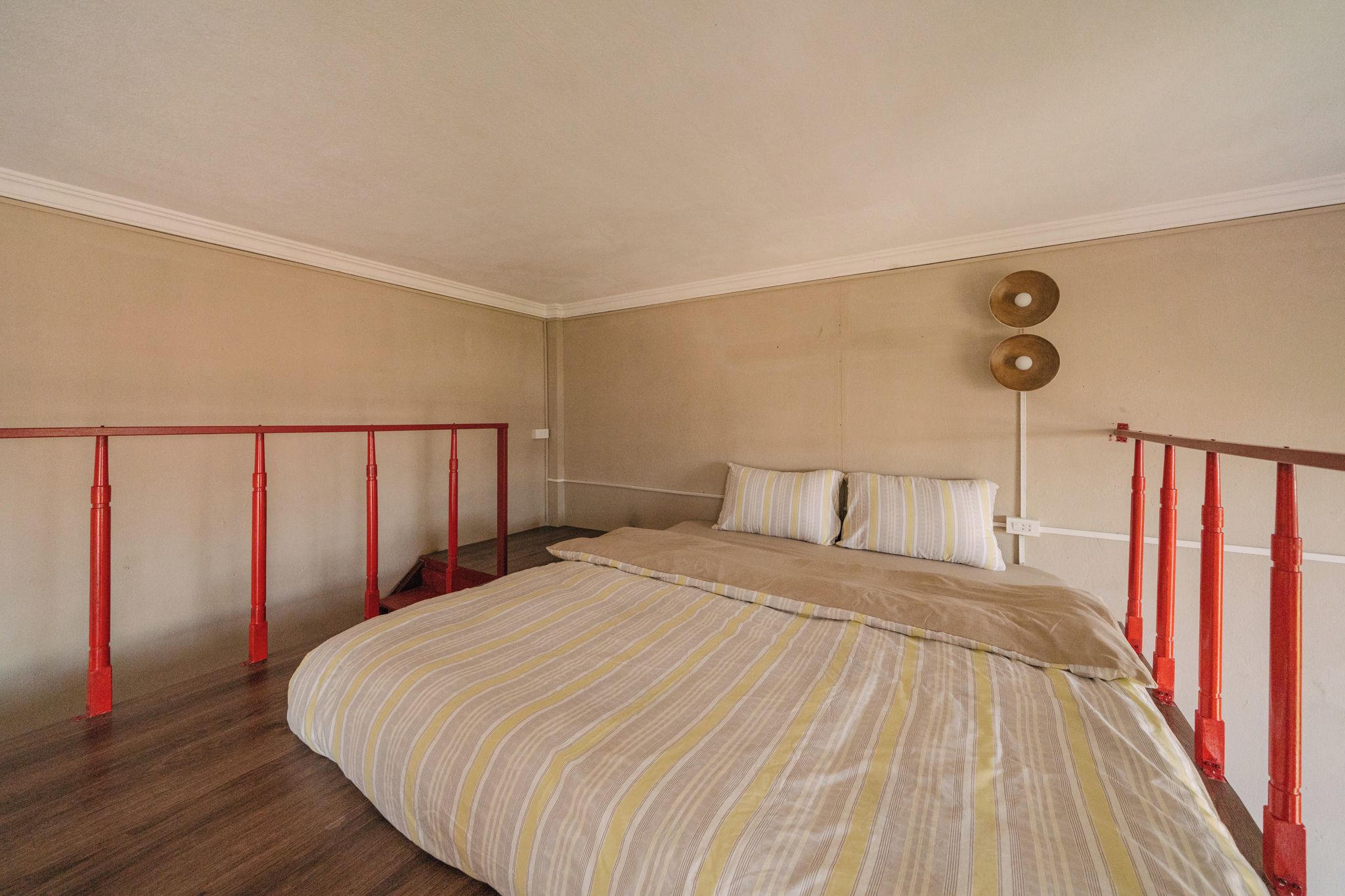 A bedroom with a bed, a red railing, and a light fixture.