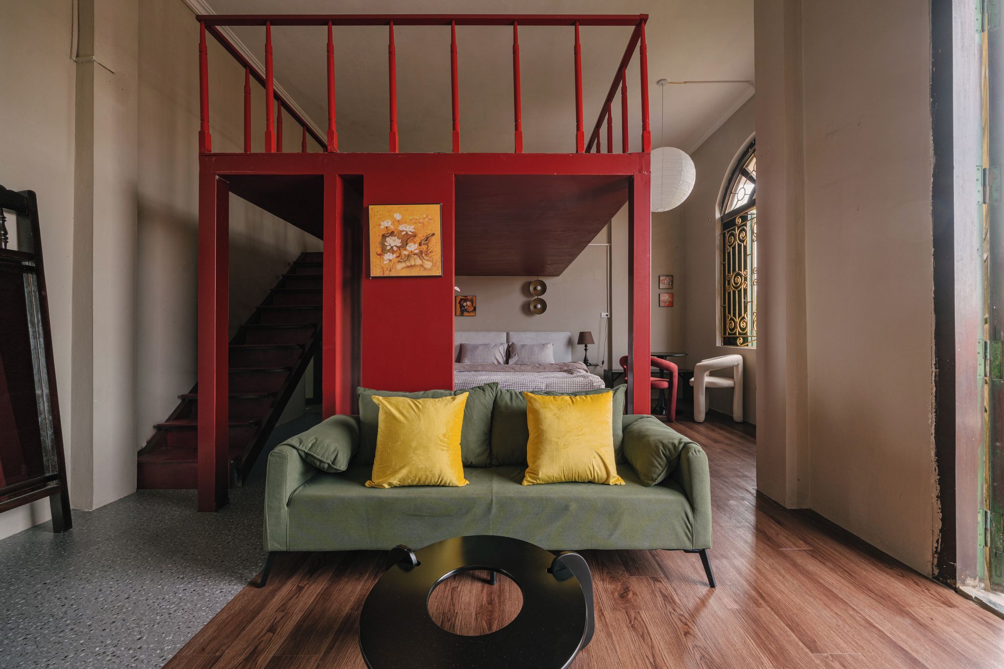 A living room with a green sofa, yellow cushions, a black coffee table, and a staircase with red railings leading to an upper level.