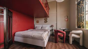 A bedroom with a bed, a chair, a table, and a window with decorative iron bars.