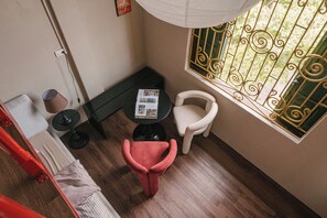 A room with a wooden floor, a black table with a magazine, a white chair, and a red chair. - Toffee Homestay Ninh Binh (Hoa Lu)