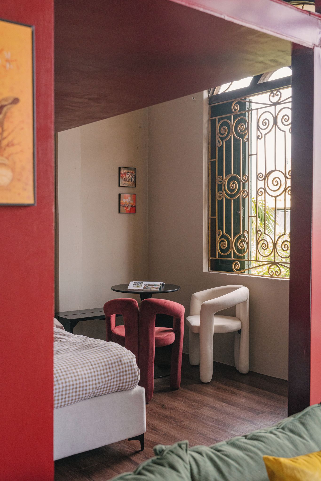 Une pièce de taille modeste, comprenant un lit, une petite table, deux chaises et une fenêtre ornée de barreaux en métal décoratifs.