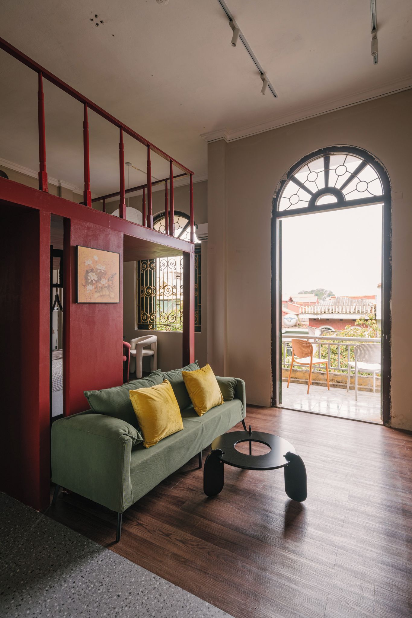 A spacious living area with a green sofa, a small round table, and a view through a large arched window.