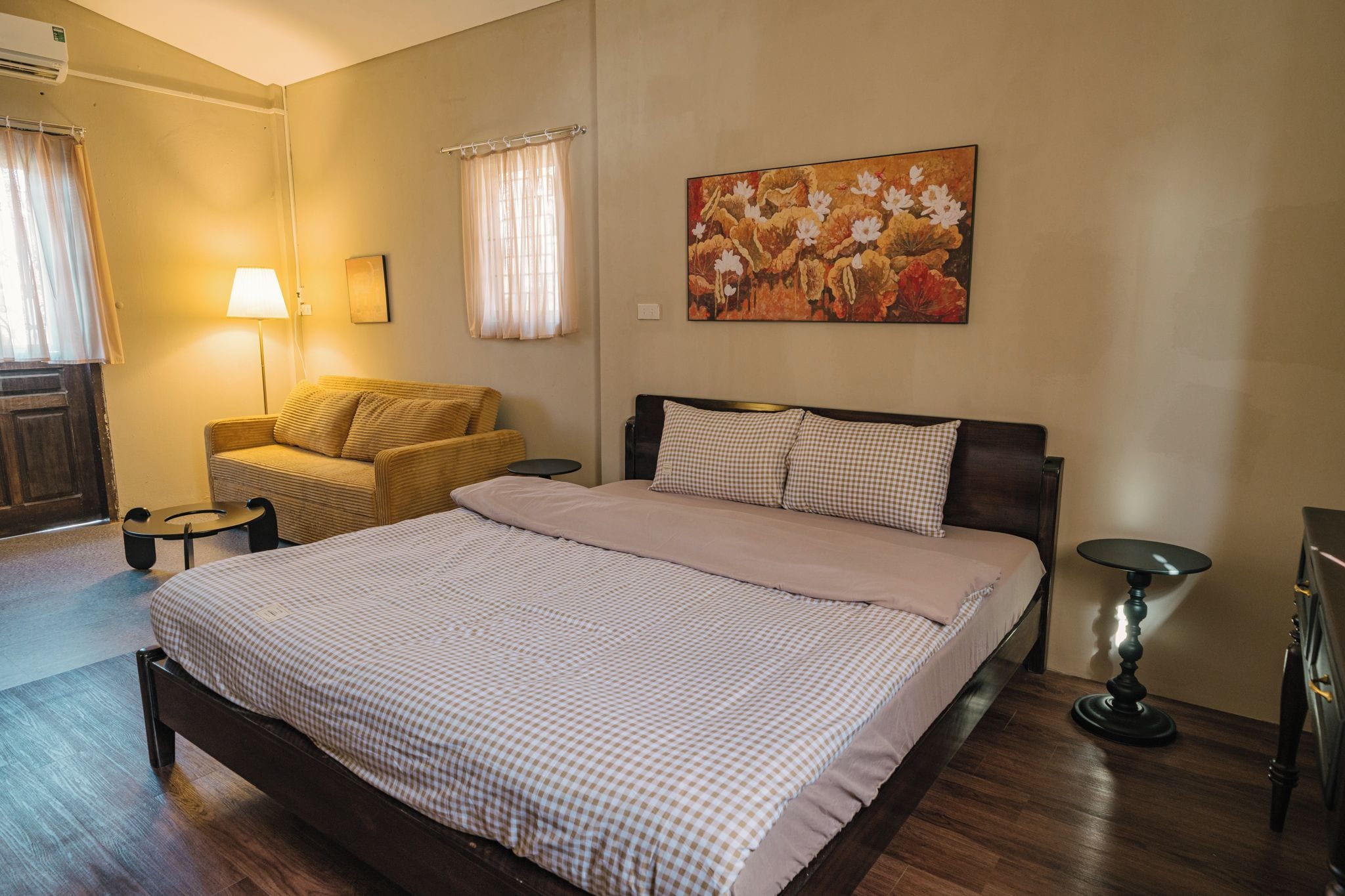 A bedroom with a bed, a sofa, a lamp, and a painting on the wall.