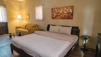 A bedroom with a bed, a sofa, a lamp, and a painting on the wall.