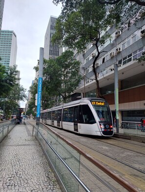 A modern tram on tracks with a clear sky, surrounded by urban buildings and trees.