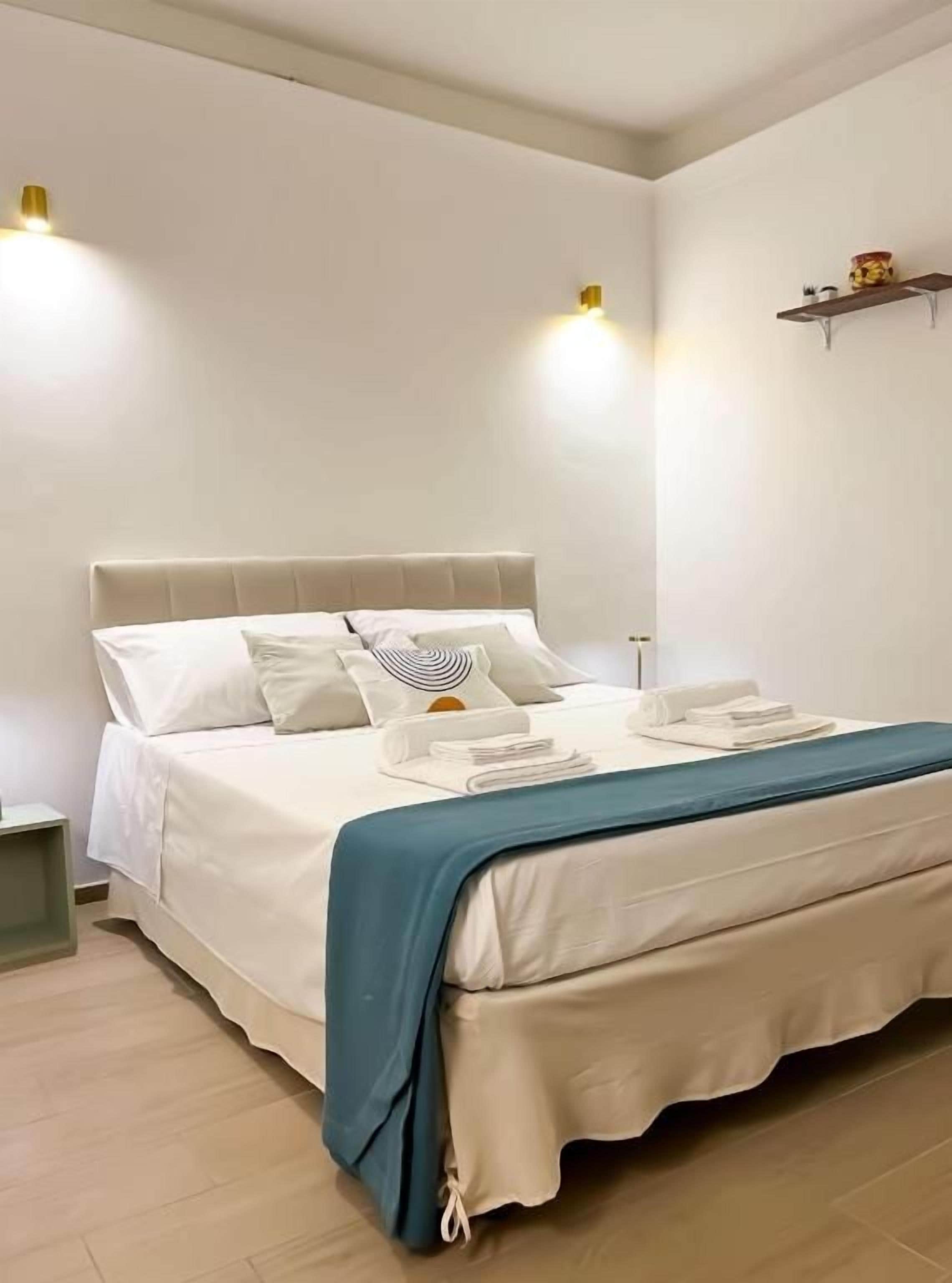 A neatly made bed with a white headboard, a blue throw blanket, and a small bedside table with a lamp.