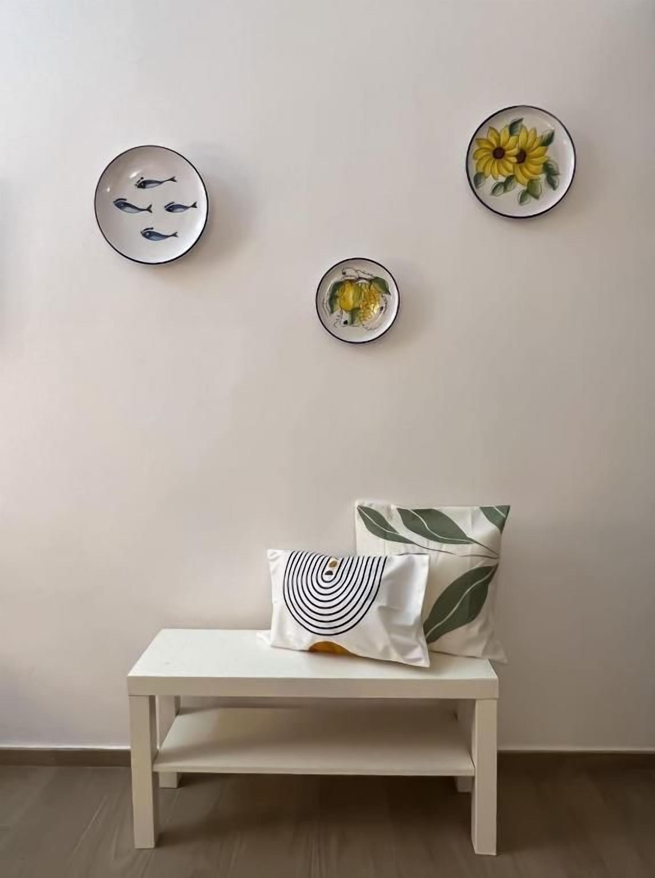 A white bench with a pillow and two wall-mounted plates with fish and a flower design.