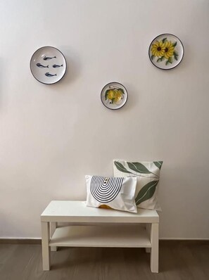 A white bench with a pillow and two wall-mounted plates with fish and a flower design.