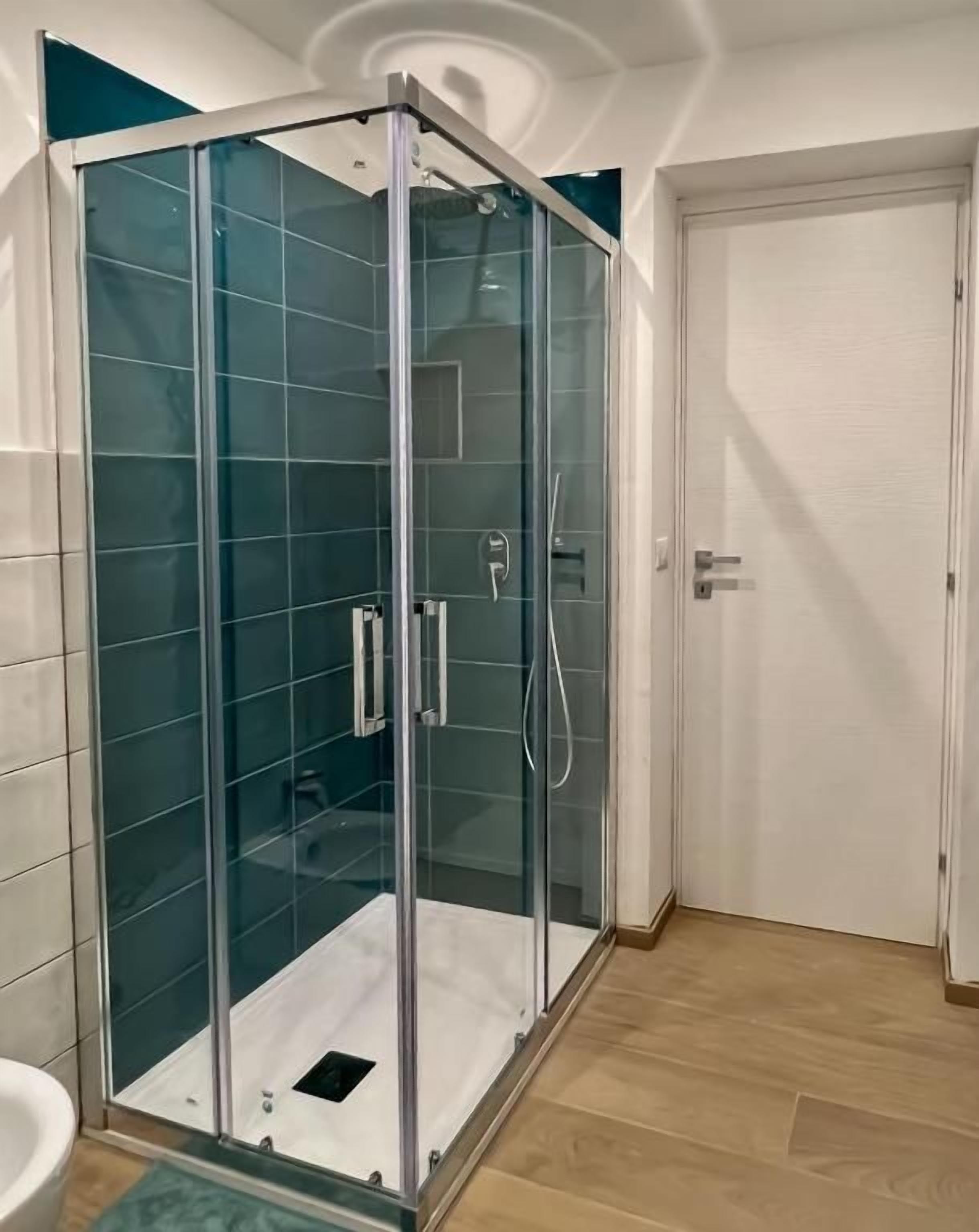Ein Duschbereich mit Glasabtrennung, einer weißen Tür und einem gefliesten Boden.