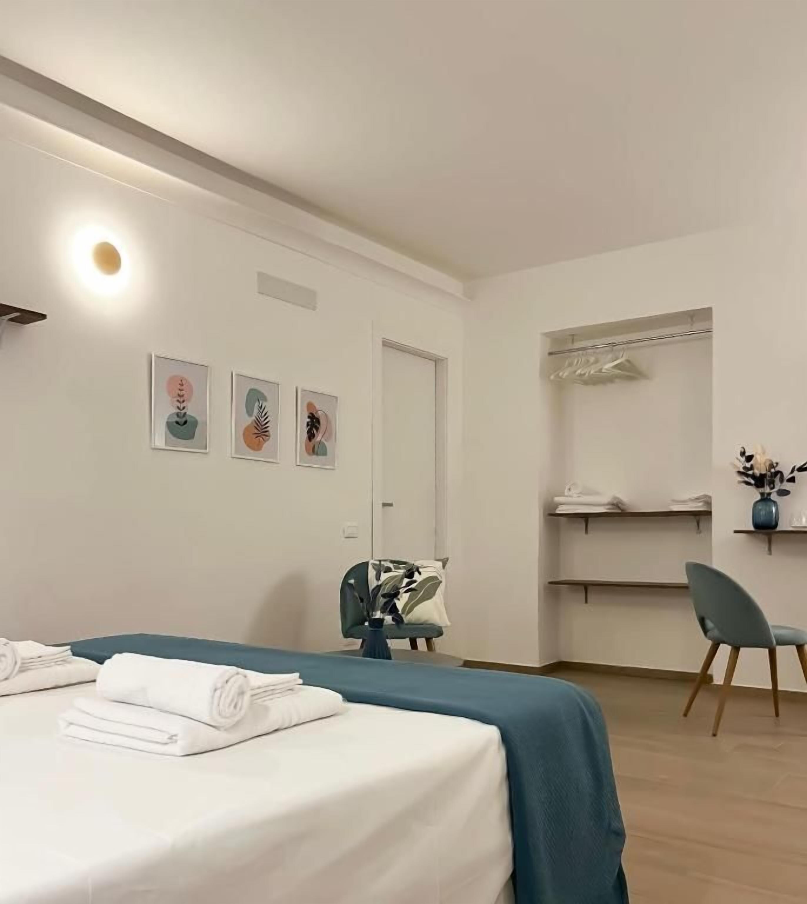 A hotel room with a bed, a desk, a chair, and artwork on the wall.