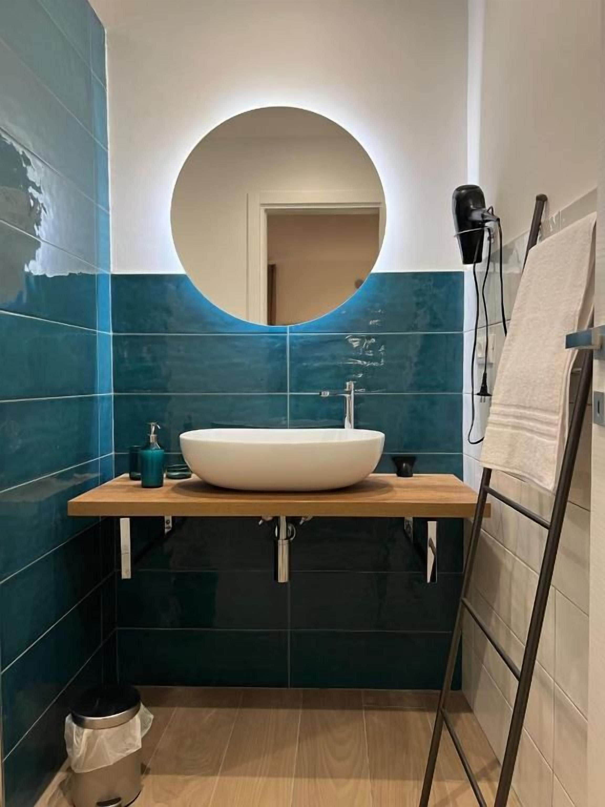 Een badkamer met een ronde spiegel, een witte wastafel en een handdoekrek.