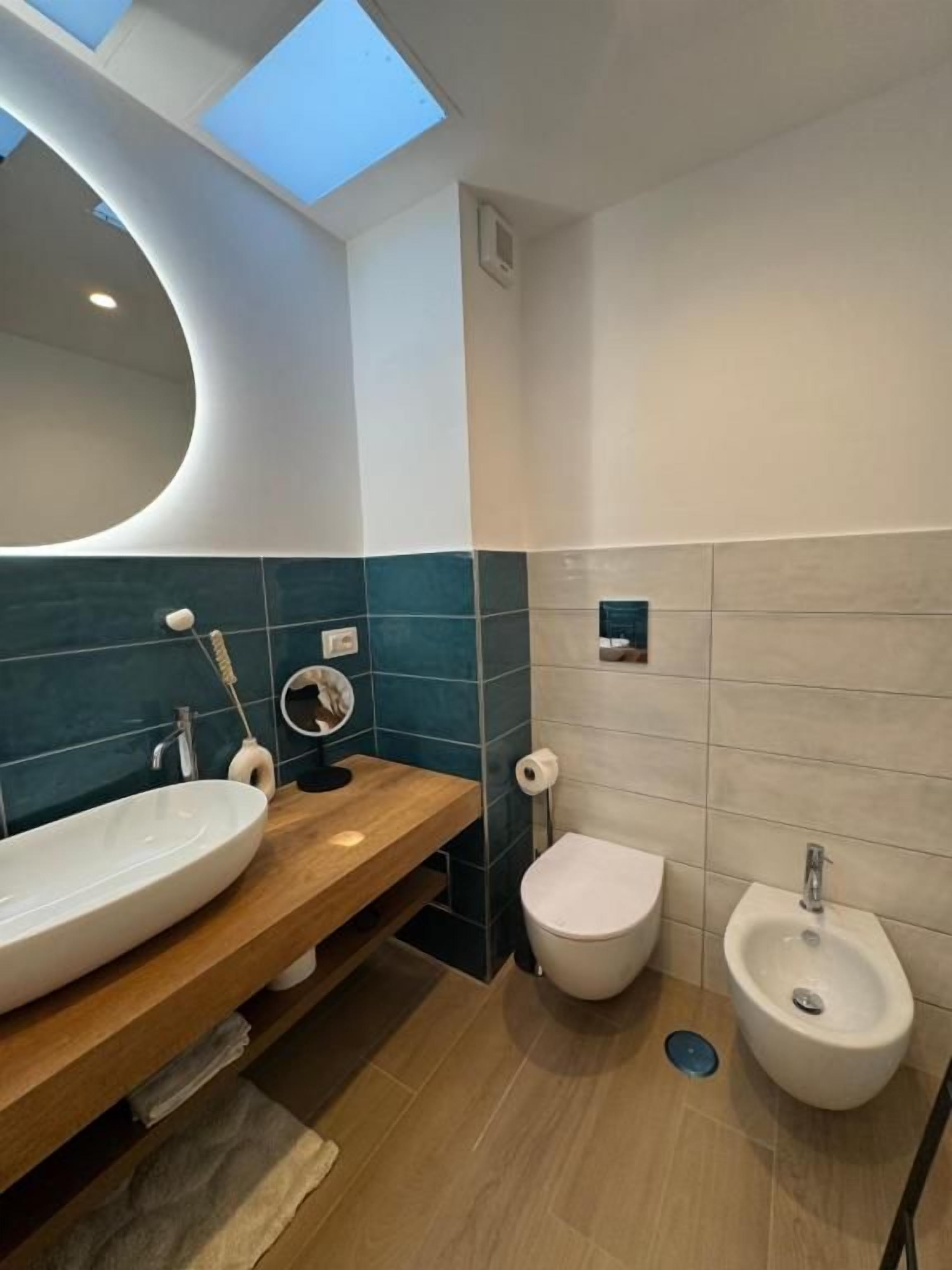 A modern bathroom with a skylight, a large oval sink, a toilet, and a bidet.