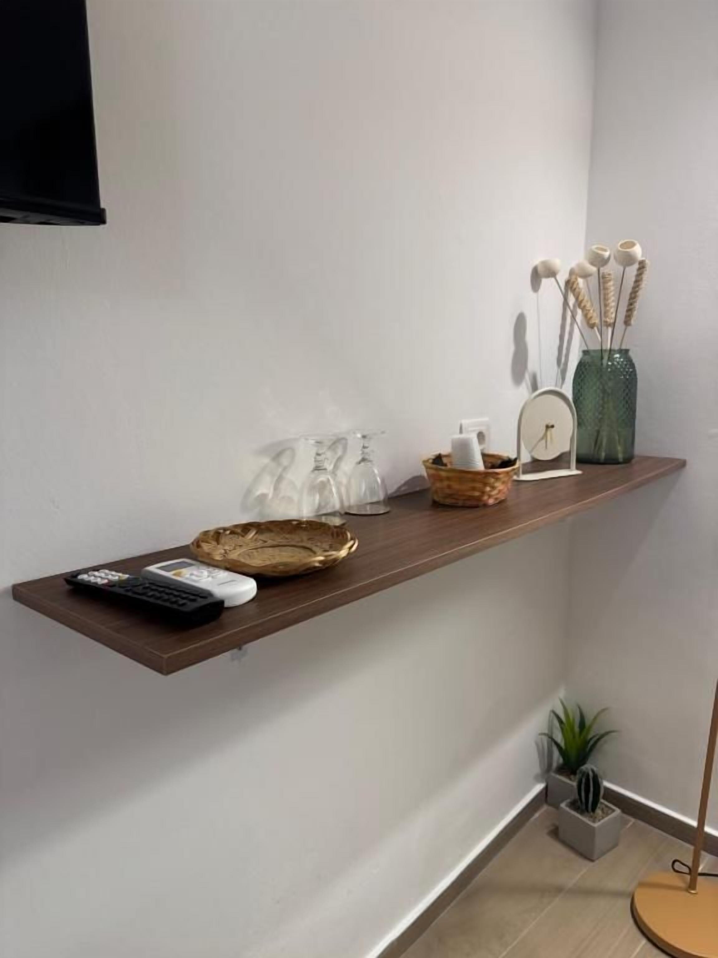 Een houten plank met afstandsbedieningen, een decoratieve schaal en een vaas met gedroogde planten.