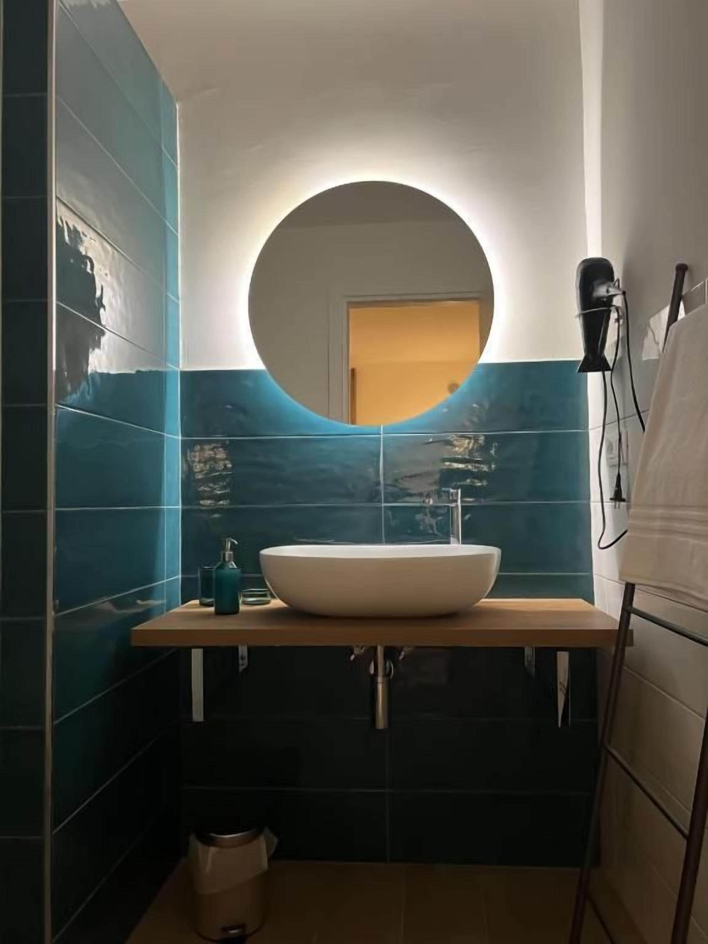 Une salle de bain avec un miroir rond, un lavabo blanc et un porte-serviettes.