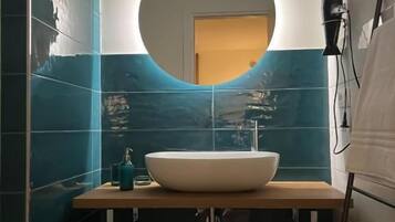 Une salle de bain avec un miroir rond, un lavabo blanc et un porte-serviettes.