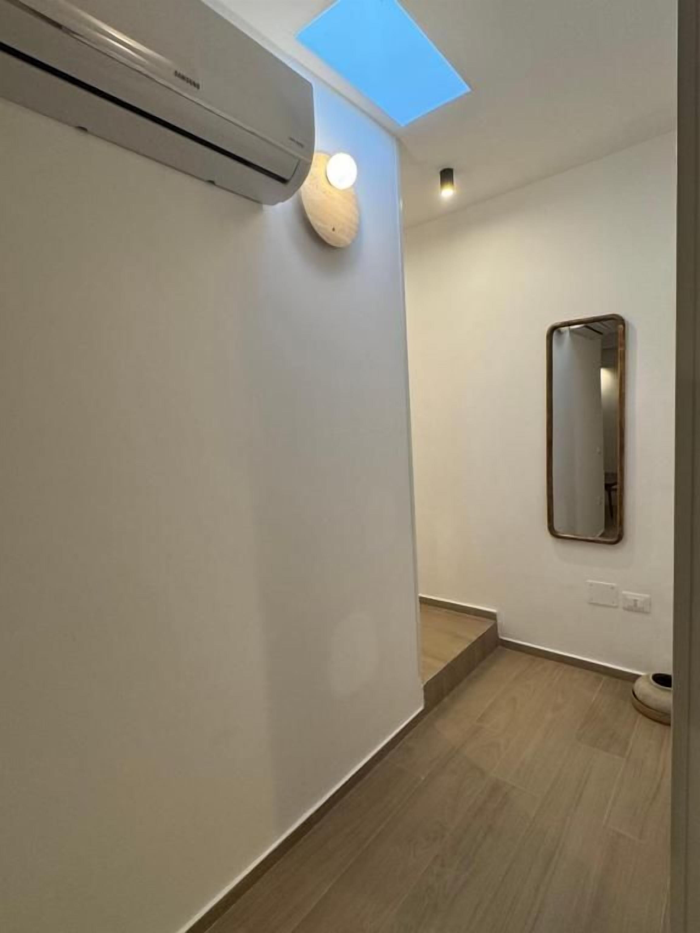 A hallway with a skylight, a wall-mounted mirror, and a light fixture.