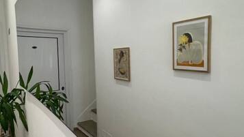 A hallway with a white door at the end, a staircase, and two framed pictures on the wall.