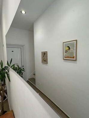 Un pasillo con una puerta blanca al fondo, una escalera y dos cuadros en la pared.