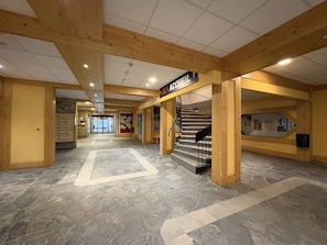 A spacious lobby with a staircase leading to an upper level, a reception desk, and a clear path marked on the floor. - Apartment at the slopes - 8 guests (La Plagne)