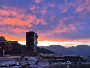 A multi-story building with a parking lot in front, surrounded by mountains and a sunset sky. - Apartment at the slopes - 8 guests (La Plagne)