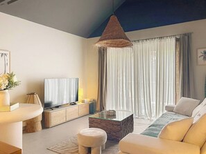 Een moderne woonkamer met een flatscreen televisie, een salontafel met glazen blad, een bank en een hanglamp.