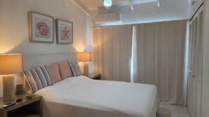 Una camera d'albergo con un letto, due lampade ai comodini, un condizionatore d'aria a parete e una tenda.