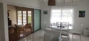 Una stanza con una porta vetrata che dà su un balcone, un tavolo da pranzo con sedie e un'ampia finestra con tende.