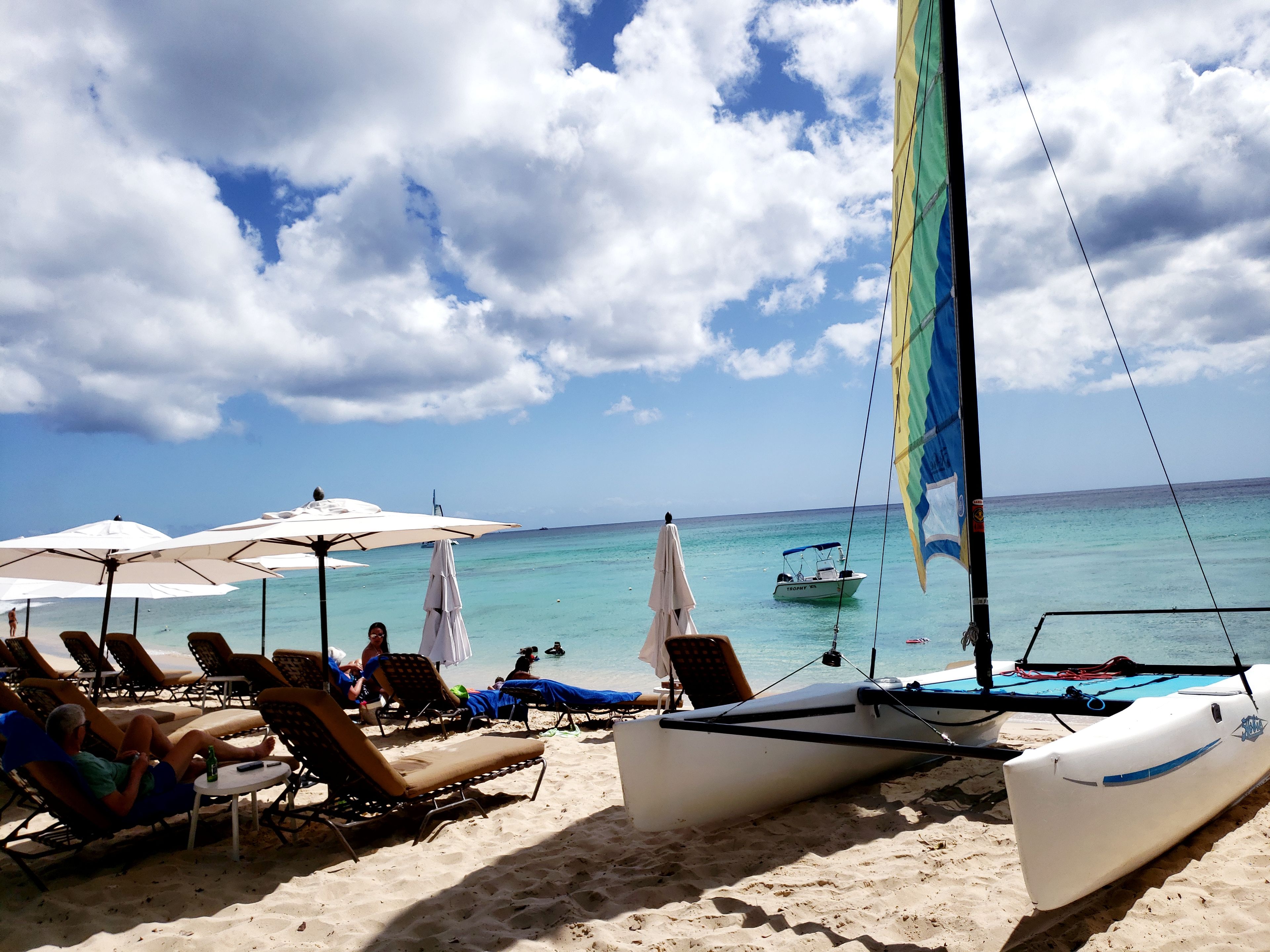 A beach with sun loungers, umbrellas, and a sailboat.