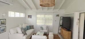 A living room with a white sofa, a glass coffee table, and a television on a wooden stand. - Welcoming 3-bedroom house that is a 4 min walk to beach (Prospect)