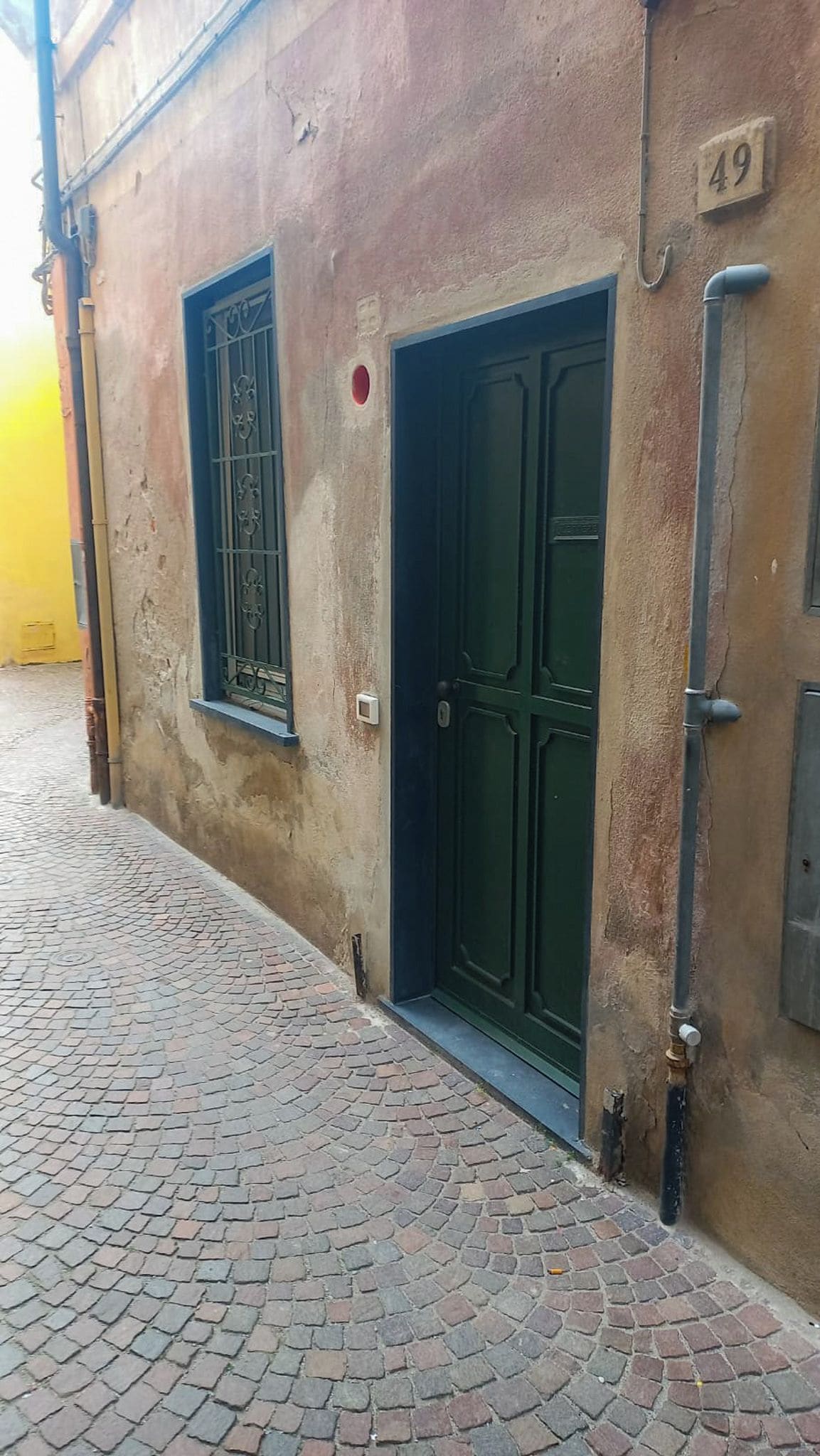 Un bâtiment situé sur une rue pavée, avec une porte verte et une fenêtre ornée de barreaux en métal.