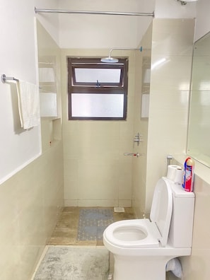 Casa de banho pequena e compacta, com chuveiro, sanita e janela.