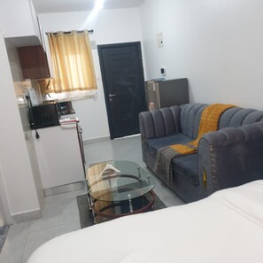 Un espacio habitable compacto con un sofá, una mesita de vidrio, un mueble pequeño y una puerta.