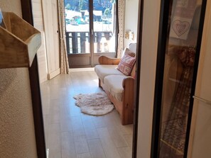 Quarto com um banco de madeira, um tapete felpudo branco e vista para uma varanda com guarda-corpo.