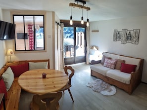 Ein gemütliches Wohnzimmer mit einem Holzesstisch, einer Couch und einem großen Fenster mit Vorhängen.